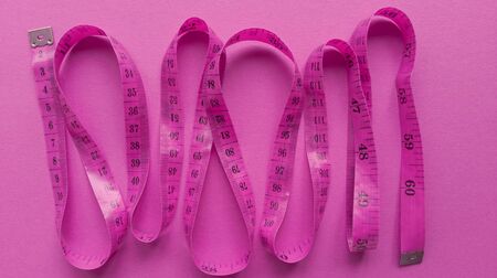 Pink centimeter on pink background. Simple flat lay with pastel texture. Fitness concept. Stock photography.の写真素材
