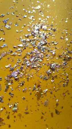 Foil pieces on yellow background with multi colored shine. Abstract fashion stock macro photo.の写真素材