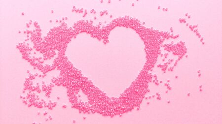 Hand made pink heart of beads on pastel texture background. Flat lay with copy space. Stock photo.