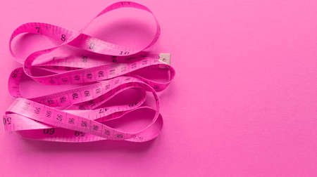 Pink centimeter on pink background. Simple flat lay with pastel texture. Fitness concept. Stock photography.の写真素材