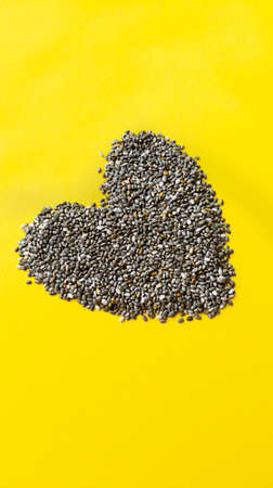 Shape of heart from chia seeds on yellow background. Simple flat lay with pastel texture. Healthy...