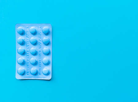 A blister of blue pills on blue background. Monochrome simple flat lay with pastel texture with copy...