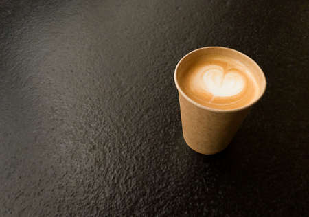 Craft cup of coffee with heart shape. Copy space on black textured table.