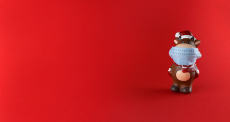 Ceramic statuette of Ox in medical mask on red background with copy space. Symbol of new year 2021.の写真素材