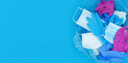 Medical pandemic coronavirus waste, face masks and latex gloves in garbage bag on a blue background...