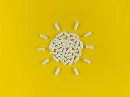 Sun shape made from white pills capsules on a yellow backdrop.