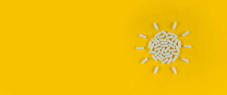 Sun shape made from white pills capsules on a yellow backdrop with copy space.