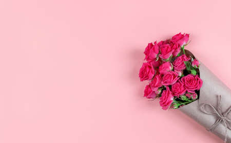 Bouquet of small flowered roses wrapped in craft paper on pink background with copy space.の写真素材