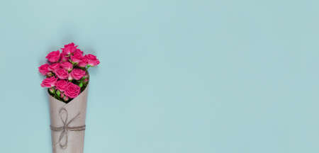Bouquet of small flowered pink roses wrapped in craft paper on a blue background with copy space.の写真素材