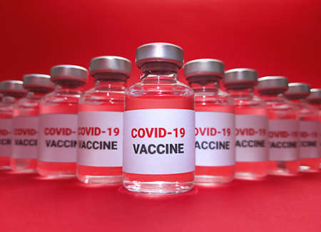 Many vials with covid 19 vaccine on red background.の写真素材