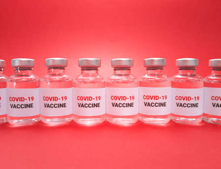 Many vials with covid 19 vaccine in a row on red background.の写真素材
