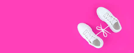 Pair of white sport shoes connected with laces bow on pink background. Simple flatlay with copy space.の写真素材