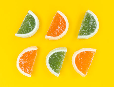 Orange and green marmalade citrus slices in sugar on yellow background.