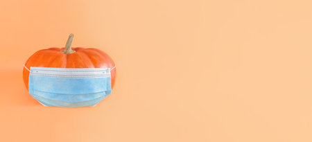 Orange pumpkin in blue medical mask on a beige background, wide banner with copy space.の写真素材