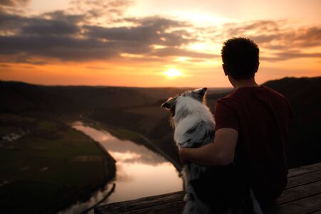 A man with a dog at sunset. walk with a pet. Australian Shepherd and owner in nature look at a beautiful view の写真素材