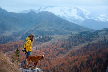 girl with a dog in the mountains. travel, Nova Scotia Duck Tolling Retriever with with a woman in a yellow jacket stand on a stone near a cliffの写真素材