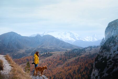 girl with a dog in the mountains. travel, Nova Scotia Duck Tolling Retriever with with a woman in a yellow jacket stand on a stone near a cliffの写真素材