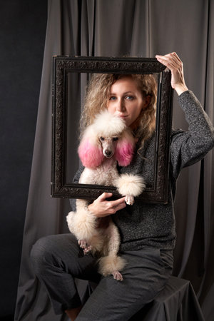 happy girl with a dog in a photo studio on gray. white Poodle and curly womanの写真素材