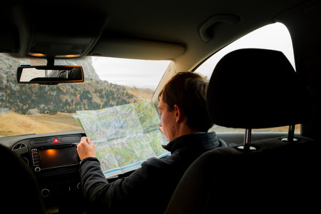 man is sitting in a car in the mountains looking at a map and studying the route. Hiking, Travel