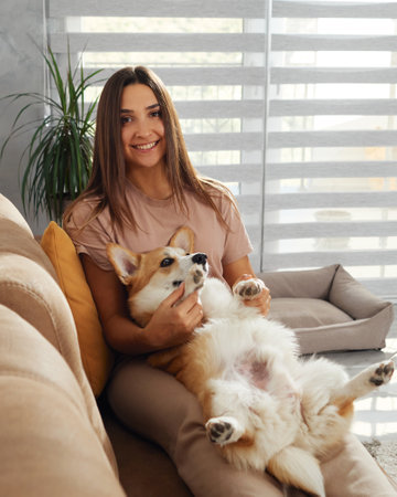 A woman relaxes with her corgi on a cozy couch at home.の写真素材