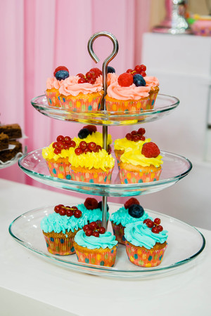 delicious pink, yellow and blue cupcakes on a three-tier glass plateの写真素材