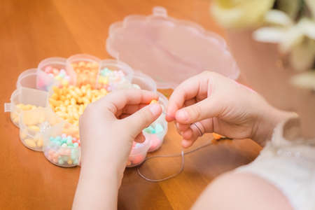 The hands of a little girl put a bead on the thread. Children's workshop on beading and needleworkの写真素材