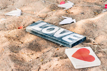 Wooden sign Love, Heart and paper cranes lie on the sandy beach. Wedding decoration on the beach in rustic styleの写真素材