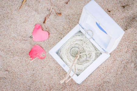Two wedding rings in a wooden box on the sand. The wedding decoration in a rustic style