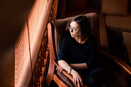 a portrait of a pensive girl sitting in a chair close to the window