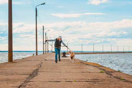 A girl and a Labrador run merrily along the sea pier. Sports and outdoor activities with Labradorの写真素材