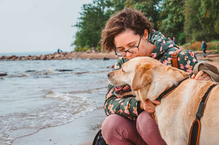 A girl kisses a dog on the head against the background of the sea. Walk with a fawn Labrador on a sandy beachの写真素材