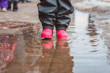 The feet of a child in pink rubber boots stomp through puddlesの写真素材