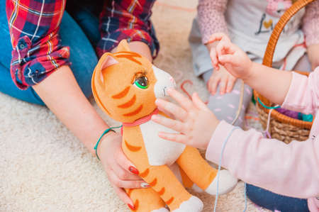 A kindergarten teacher shows children a cat. A child is stroking a soft toy in the hands of a womanの写真素材