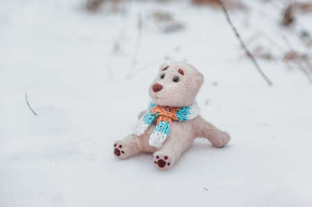 an isolated toy polar bear in a scarf sits on the snow in the winter fieldの写真素材