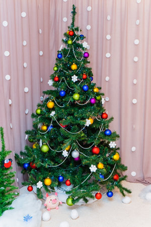 a Christmas tree decorated with colorful balloons, white beads and a glowing electric garland stands in the cornerの写真素材