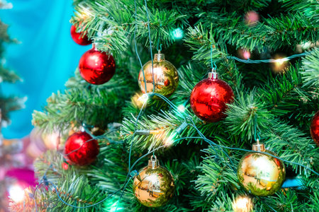 the Christmas tree is decorated with red and gold shiny balls and a glowing electric garlandの写真素材