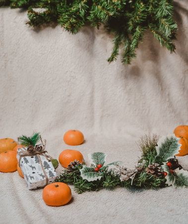 christmas white textured background with fir twigs, cones, holly leaves and berries, gifts and tangerinesの写真素材