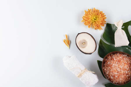 Scented sea salt and white face towel, grass pouch for massage, beutiful flower and coconut candle for relaxed mood on the green leaf.の写真素材