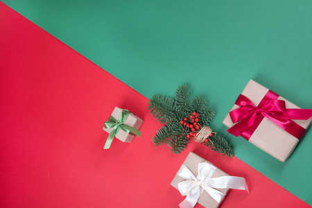 Beautiful packaging of presents with satin ribbons, craft paper and natural pine branch on red and green background.の写真素材