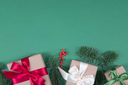 Beautiful packaging of presents with satin ribbons, craft paper on green background with natural pine branches.の写真素材