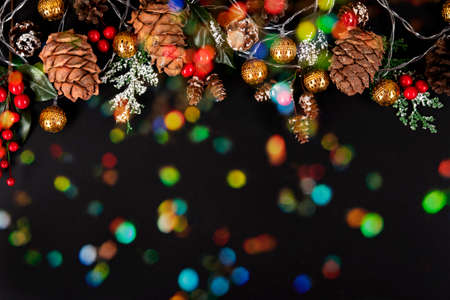Golden garland, forest pinecones, red berries and green leaves in snow on the black background with multicoloured lights.の写真素材