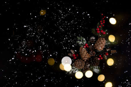 Forest pinecones, red berries and green leaves with white candle on the black background in snow and lights.の写真素材