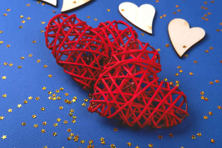 Beautiful red and wooden hearts on the cornflowerblue background in the golden star sequins. St...