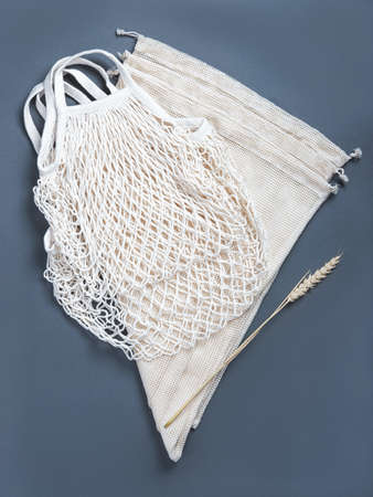 The white zero waste string bag and three string sacks for fruits, vegetables, grocery or other products on the grey background with a wheat spikelet.の写真素材