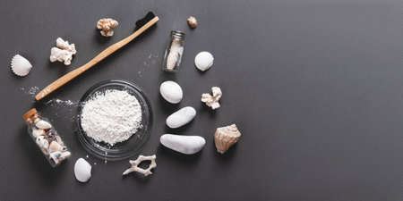 Zero waste concept for teeth cleaning. A bamboo toothbrush with a floss and toothpowder in a glass decorating with shells, stones and corals on the grey background, banner with the copyspace.の写真素材