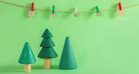Three beautiful handmade wooden fir trees and wooden snowflakes on the string on the green background with the space for your design. Christmas or New Year decoration banner.の写真素材