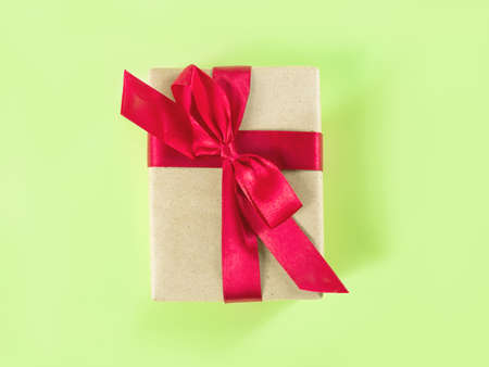 The above view on the packed present in the craft paper with the red satin ribbon on the light green...