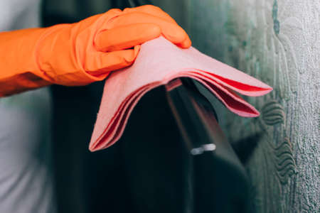the woman tidies the room by dusting the TV with a gloved ragの写真素材