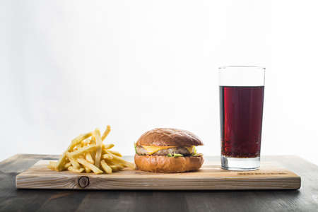 Crafting a burger with fries and a glass of soda on a boardの写真素材