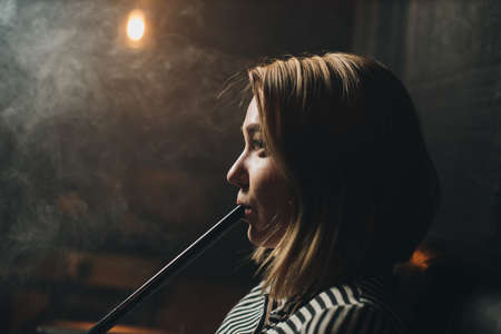 Beautiful girl 20 years old smokes a hookah on the couchの写真素材